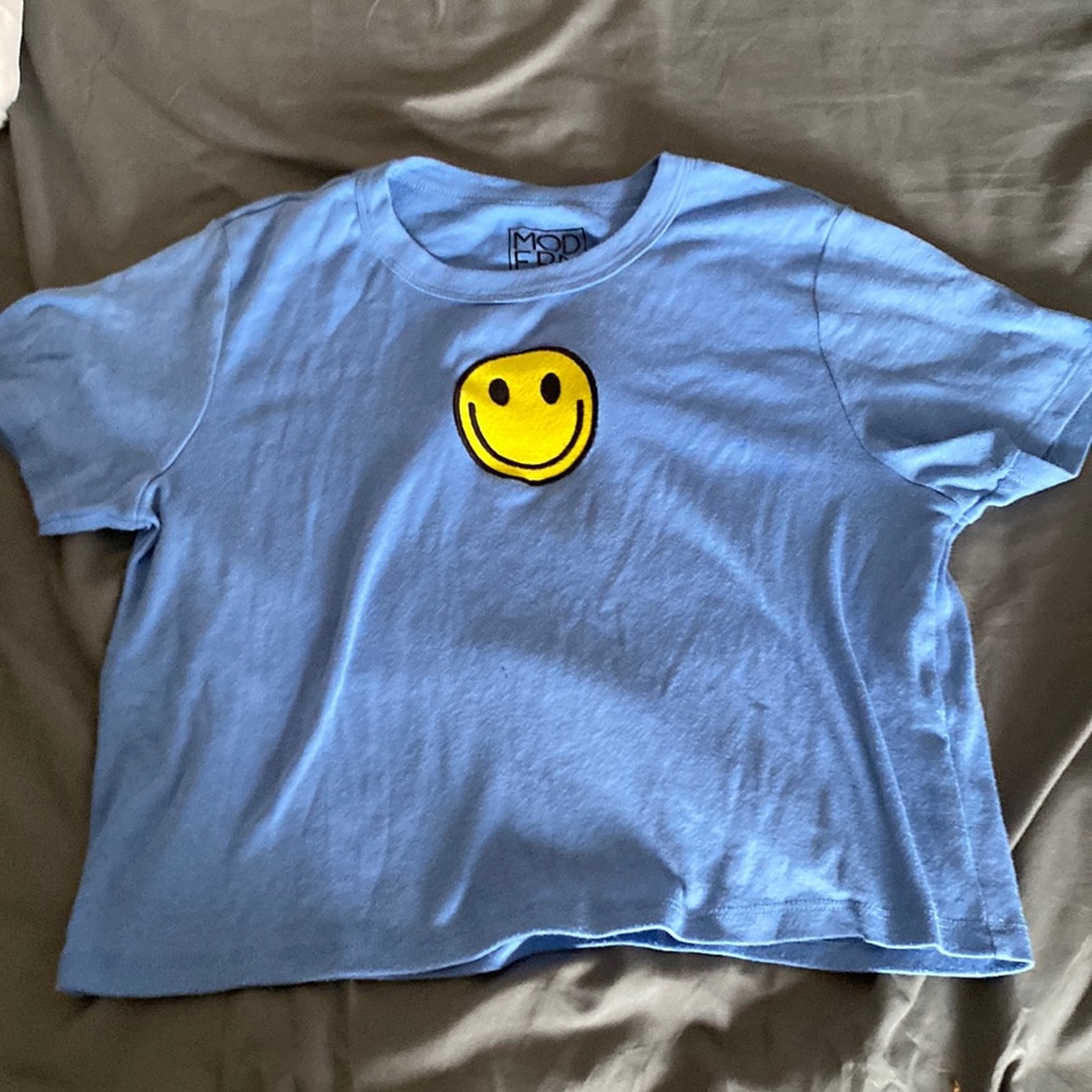 It is a blue shirt with a yellow smiley face on it